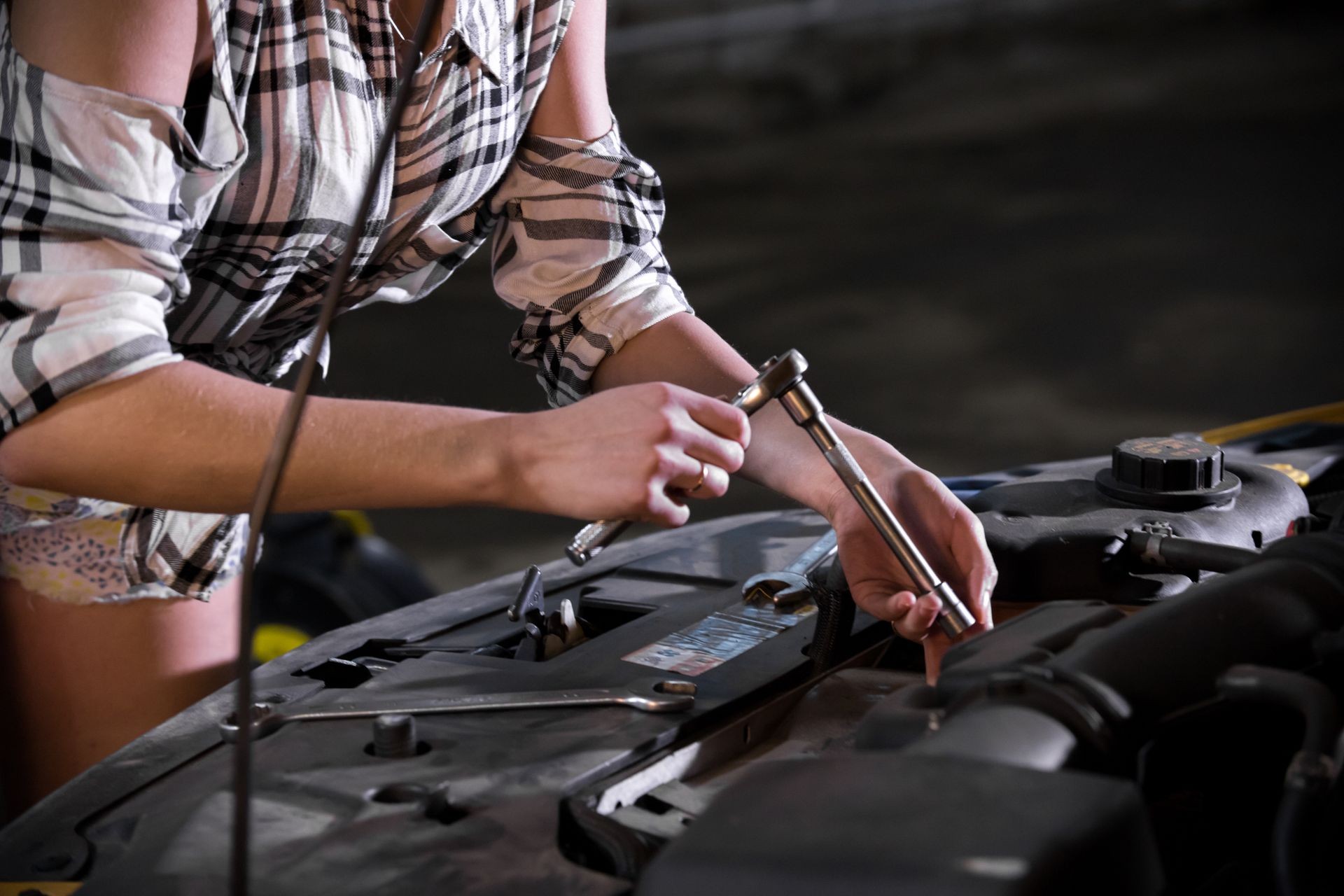 Car repair service. Young sexy woman stands in front of an opened car hood and working with a wrench